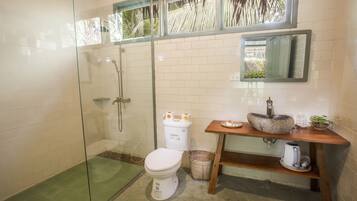 A bathroom with a glass-enclosed shower, a white toilet, a sink with a stone basin, and a mirror above the sink.