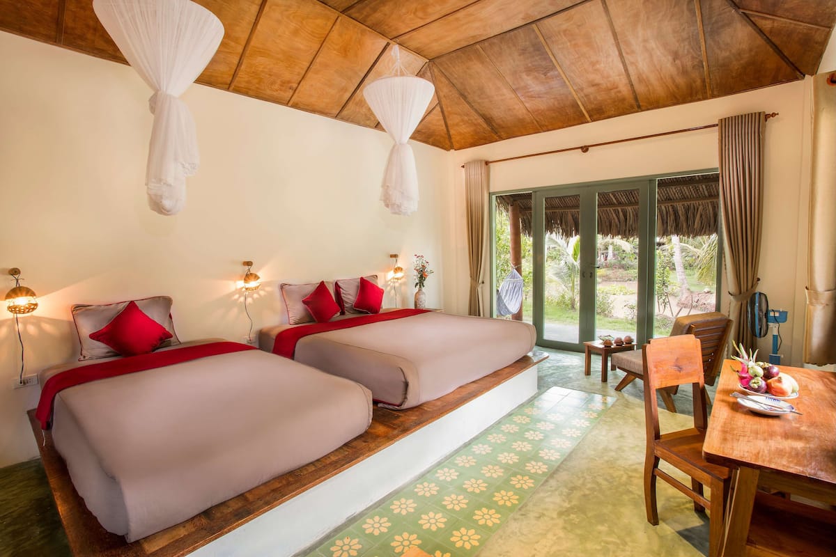 A room with two beds, a dining table, and a view of the outdoors.