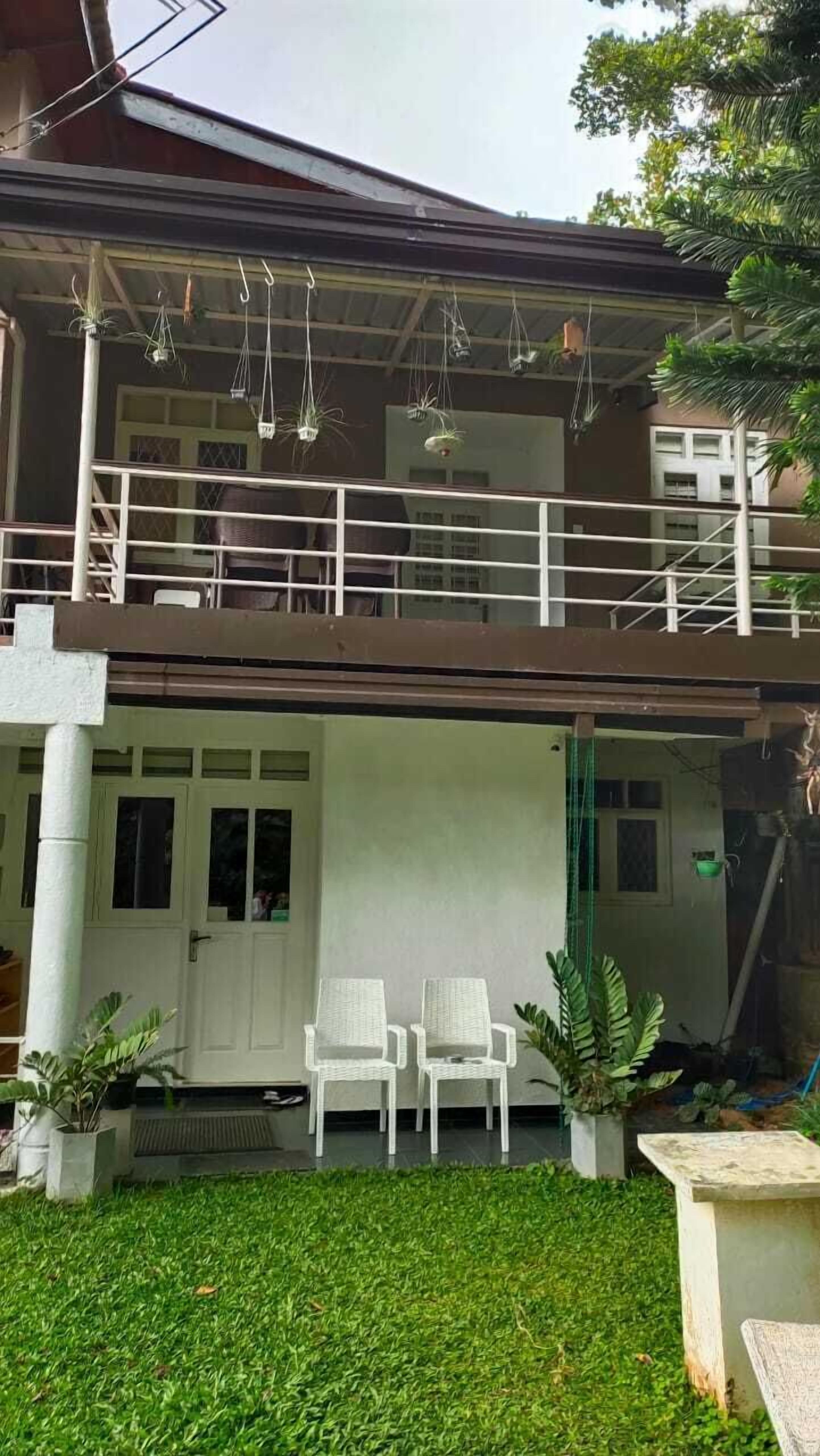 A two-story building with a balcony, white chairs, and potted plants.
