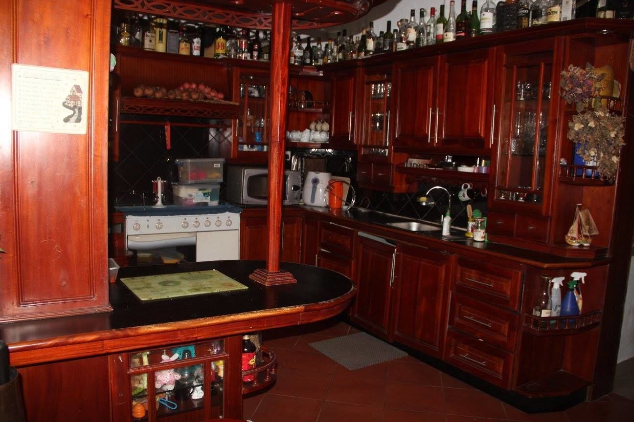Een bar met houten kasten, een aanrecht en diverse flessen.
