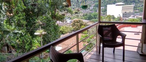 A balcony with wicker chairs, a railing, and hanging plants.