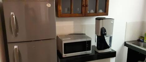 A compact kitchen with a refrigerator, microwave, coffee maker, and wooden cabinets.