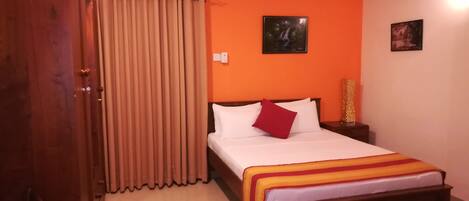 Un dormitorio con pared naranja, estructura de cama de madera, alfombra roja y colcha blanca con almohada roja.