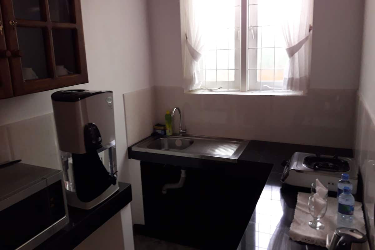 Una cocina compacta con cafetera, un lavabo y una ventana con cortinas.