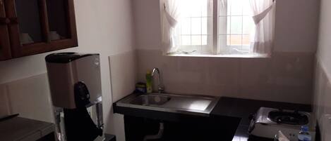 A compact kitchen with a coffee maker, a sink, and a window with curtains.