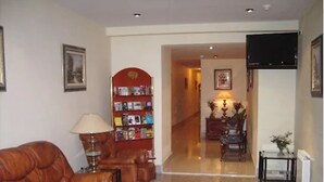 A living room with a leather sofa, a bookshelf, a lamp, and a television mounted on the wall.