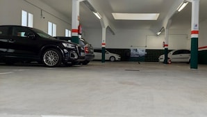 A parking garage with multiple cars parked, white walls, green and red pillars, and a tiled floor.