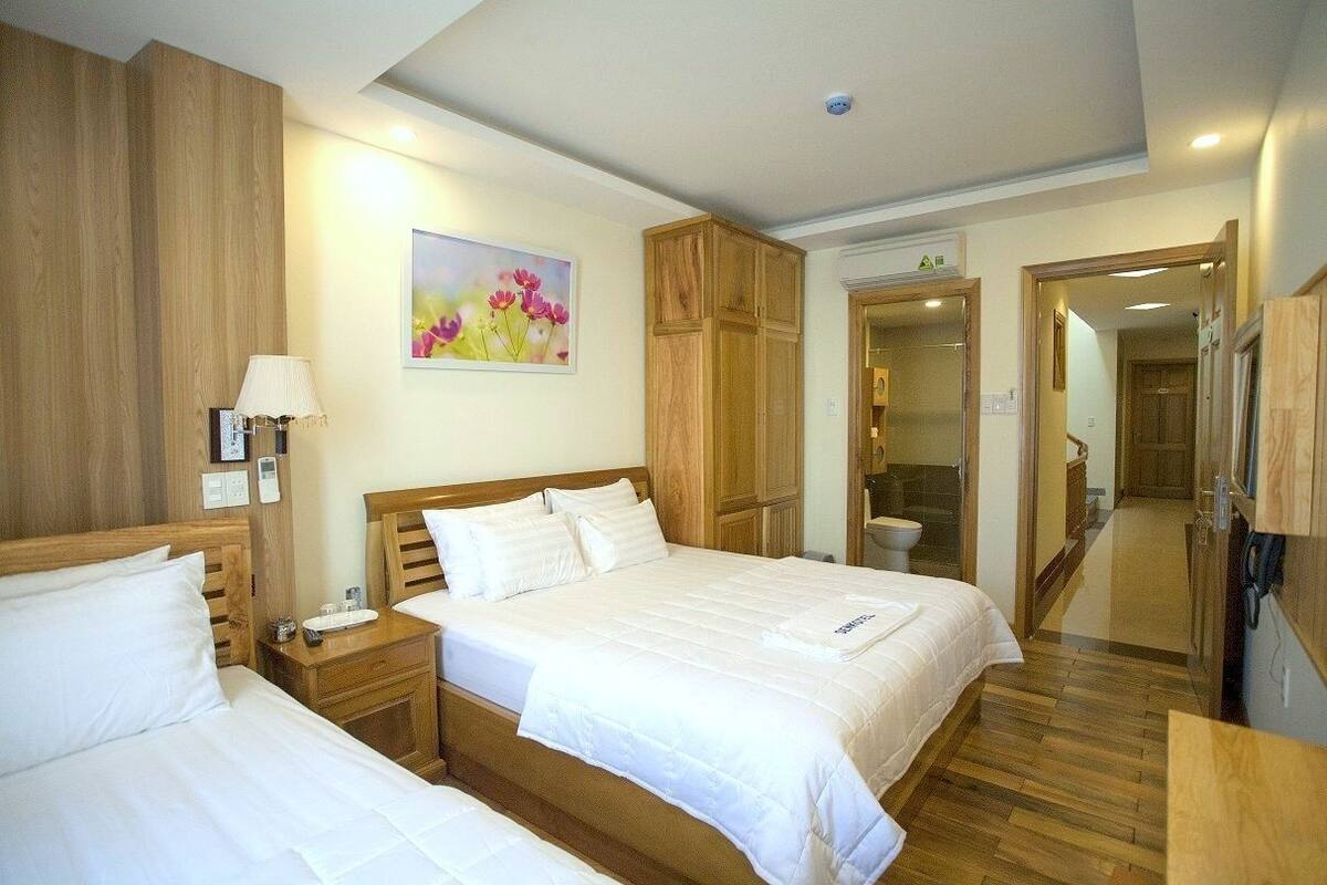 A hotel room with two beds, wooden wardrobe, a painting on the wall, and a bathroom visible through a glass door.