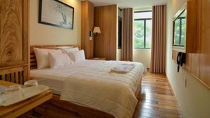 Habitación de hotel con una cama grande, suelo de madera, un escritorio con teléfono y una ventana con cortinas.