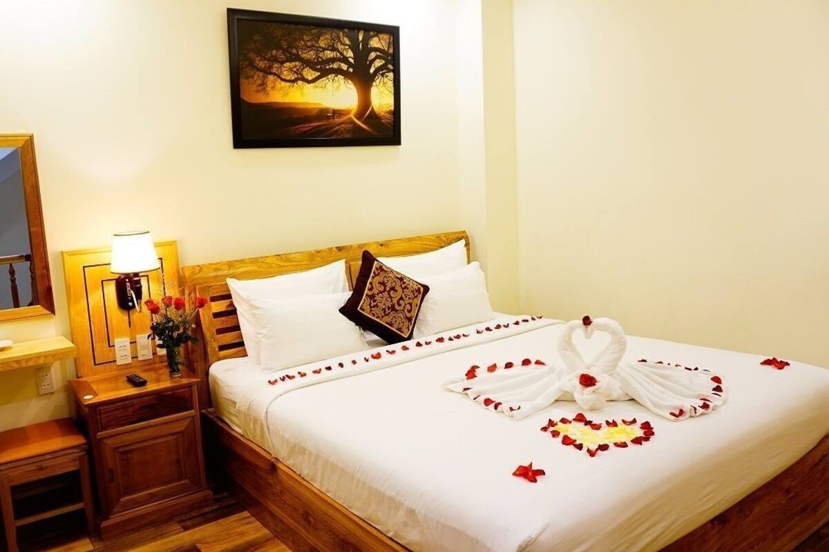 A hotel room with a wooden bed, a nightstand with a lamp, a mirror, and a painting on the wall.