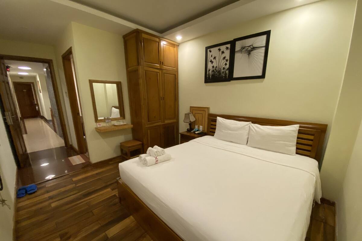 A hotel room with a large bed, wooden wardrobe, and a mirror.