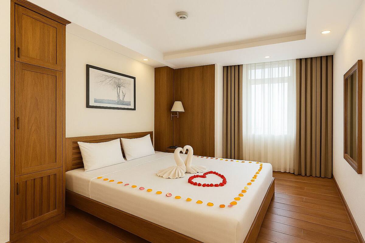 A hotel room with a large bed, wooden wardrobe, a framed picture on the wall, and a window with curtains.