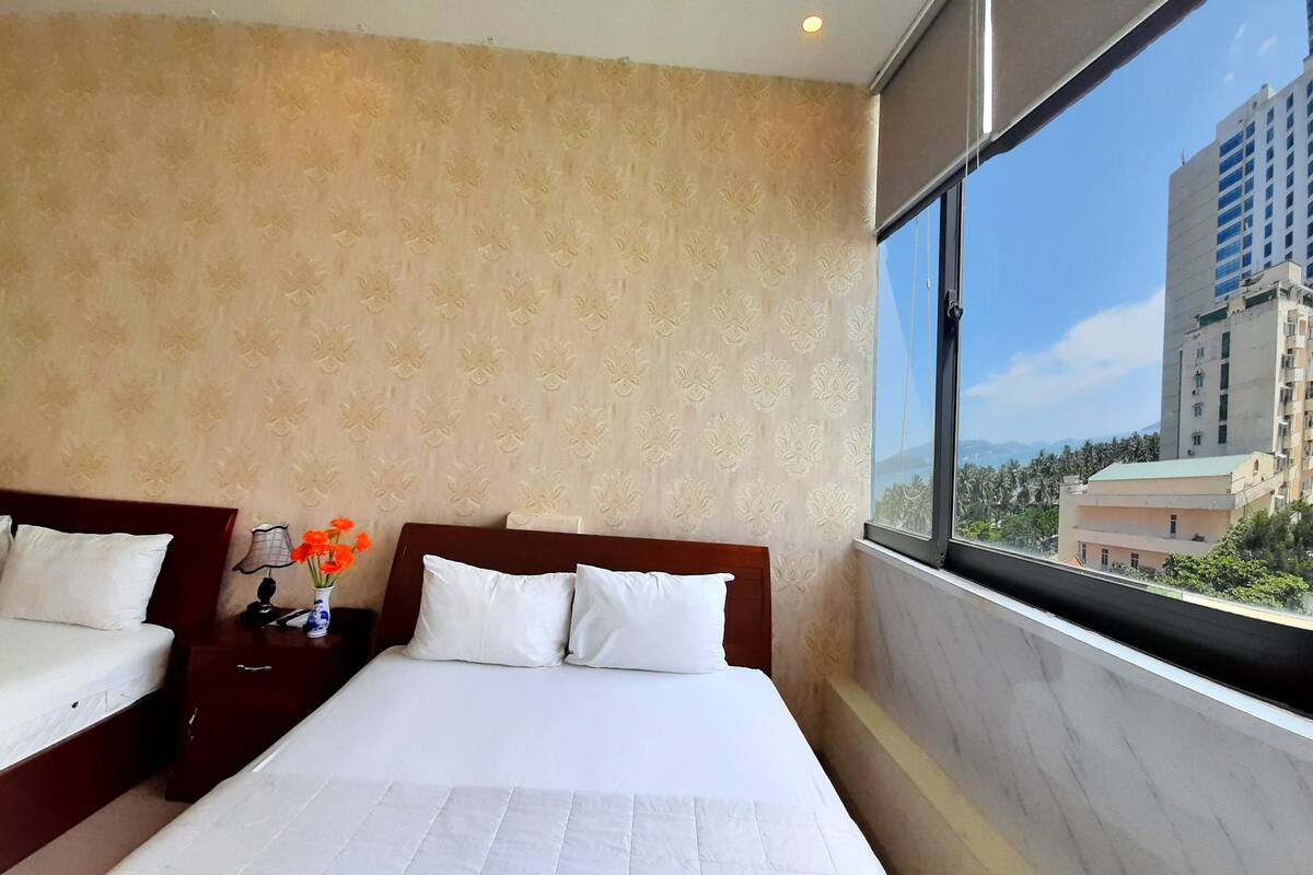 A hotel room with two beds, a large window, and a view of a cityscape.