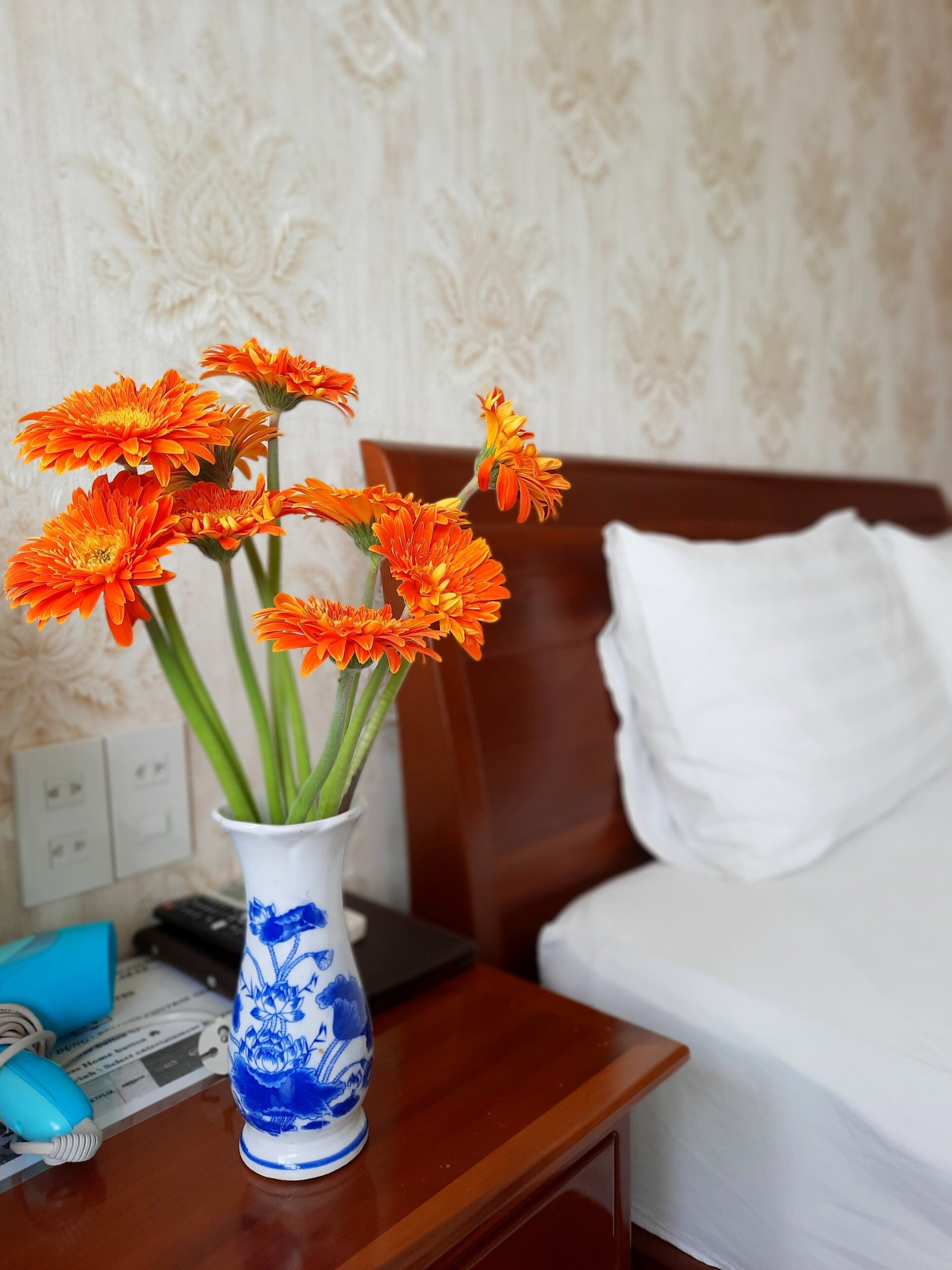 Un vaso con fiori arancioni su un comodino in legno in una camera d'albergo.