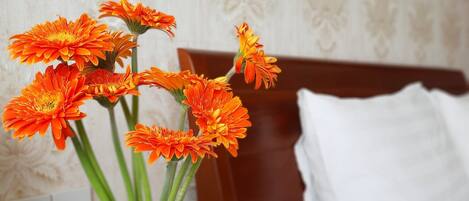 A vase with orange flowers on a wooden nightstand in a hotel room.