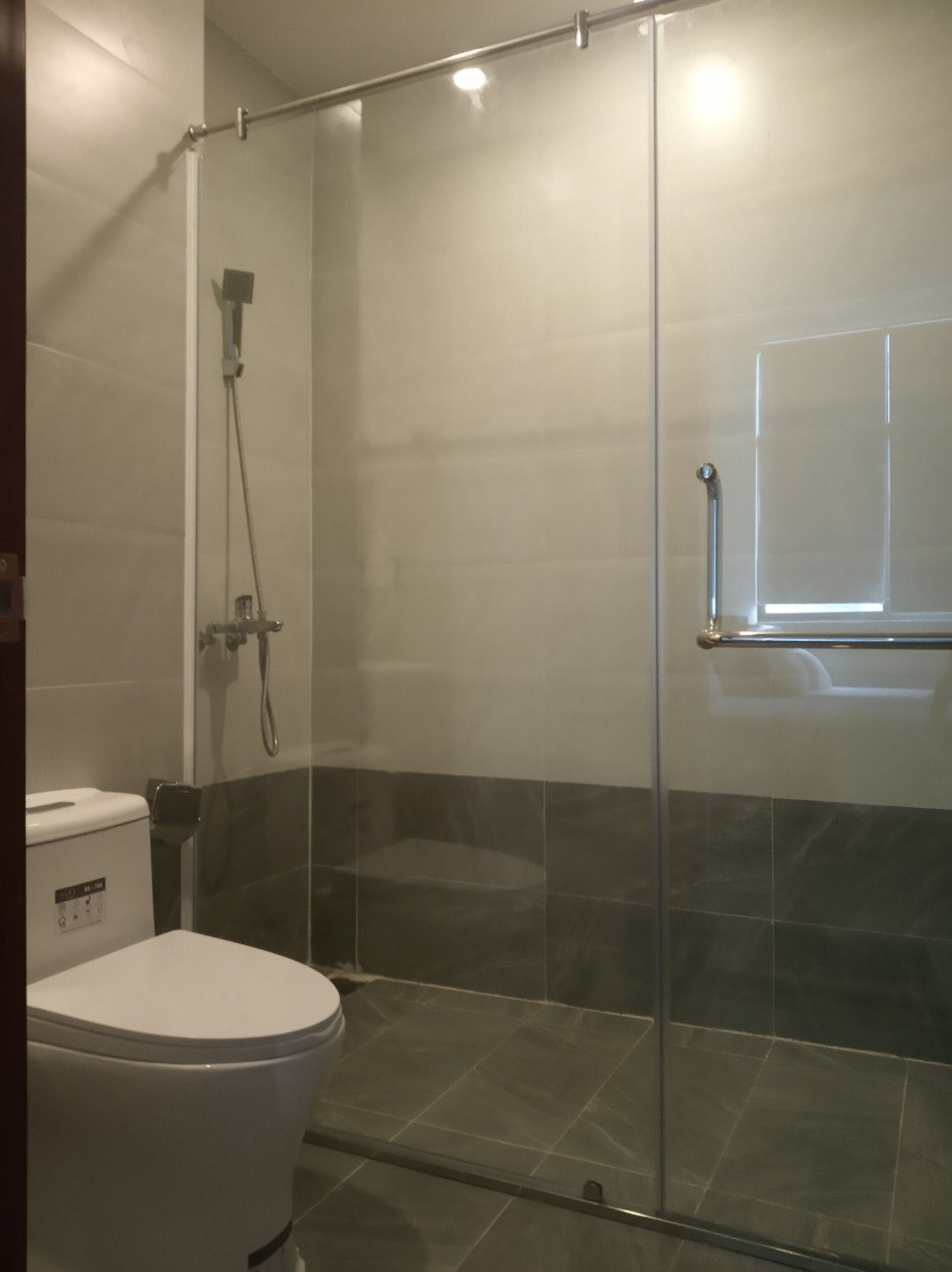 A modern bathroom with a glass shower enclosure, a toilet, and a window.