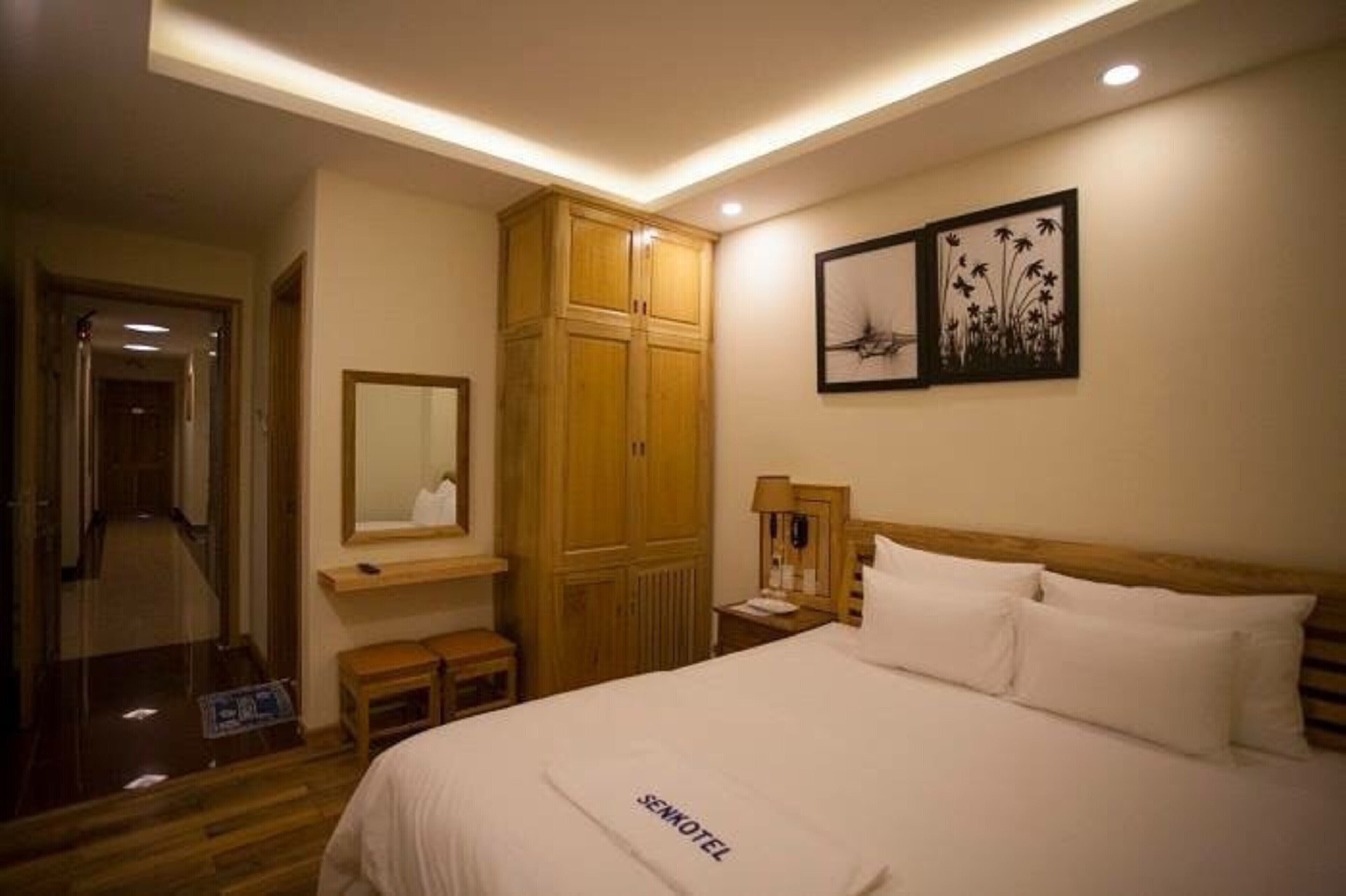 Una habitación de hotel con una cama, un armario de madera, un espejo y obras de arte en la pared.