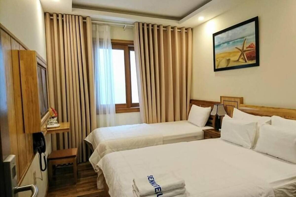 A hotel room with two beds, a desk, a telephone, and a painting of a beach scene.