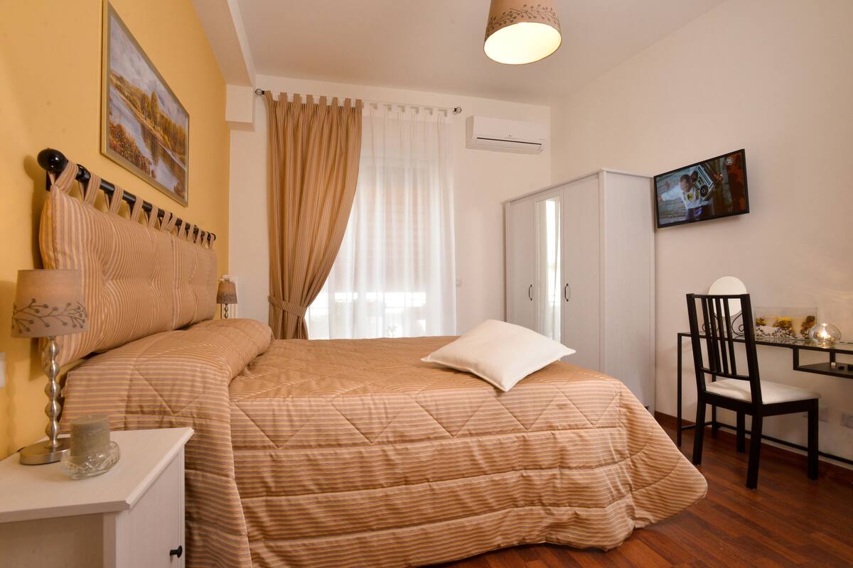 A bedroom with a bed, a nightstand, a chair, a wardrobe, and a television on the wall.
