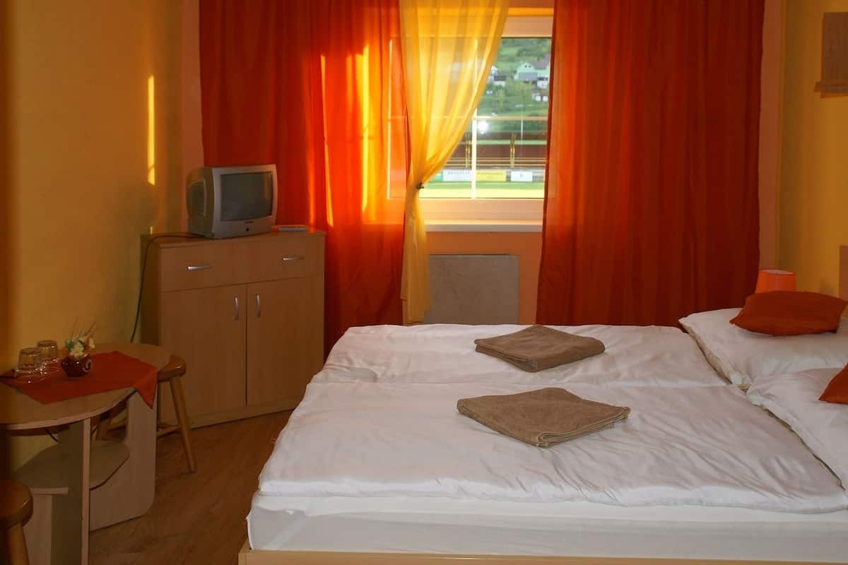 A hotel room with a bed, two pillows, a TV on a wooden cabinet, and a window with curtains.