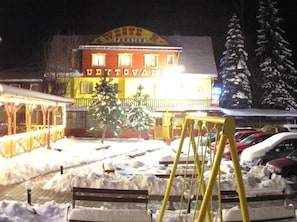 Un bâtiment avec une enseigne indiquant « VESTE N. PENZION » et un espace de stationnement dont le sol est recouvert de neige.