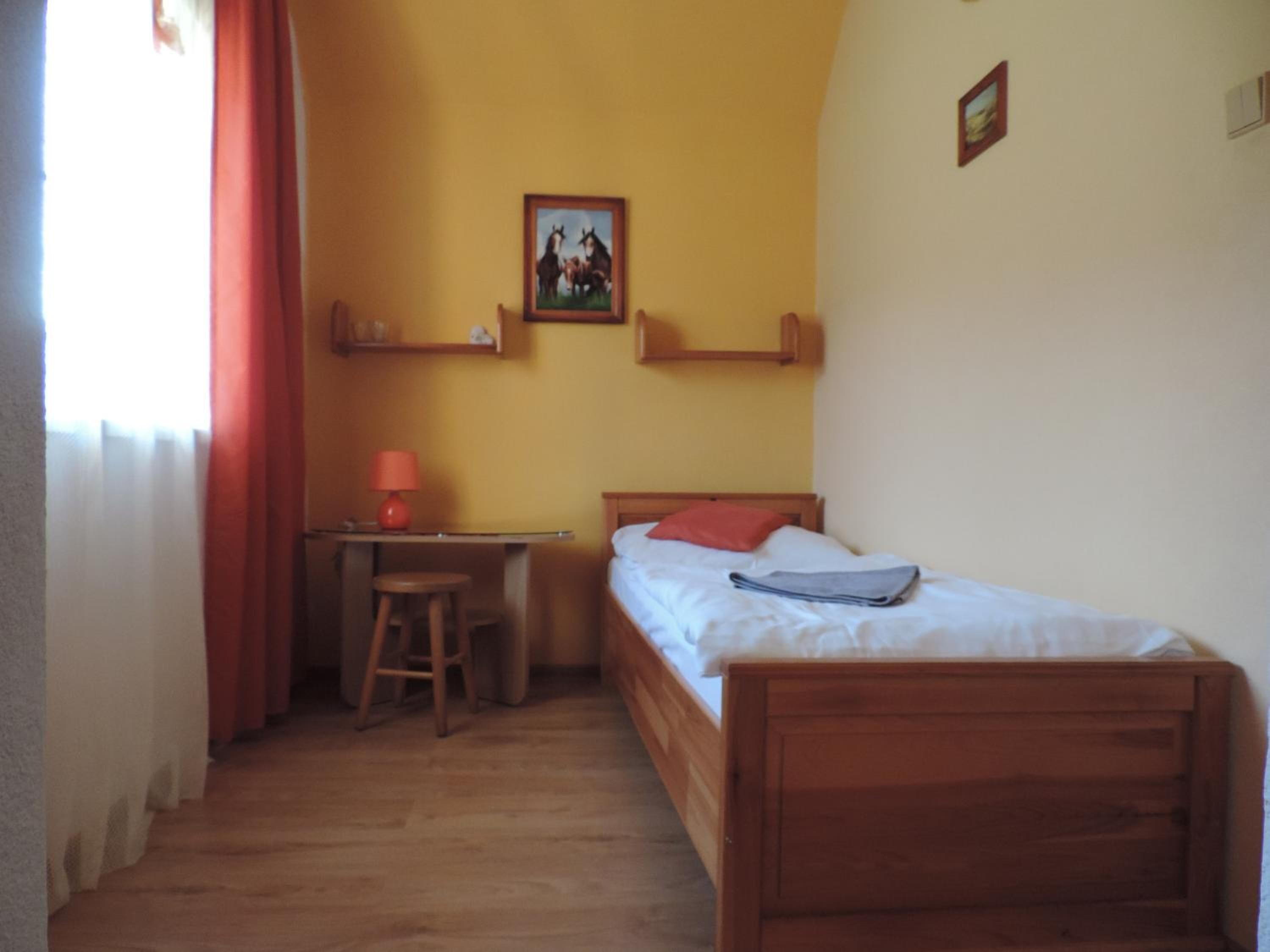 Una habitación pequeña y acogedora con una cama de madera, un escritorio con silla y una mesita.