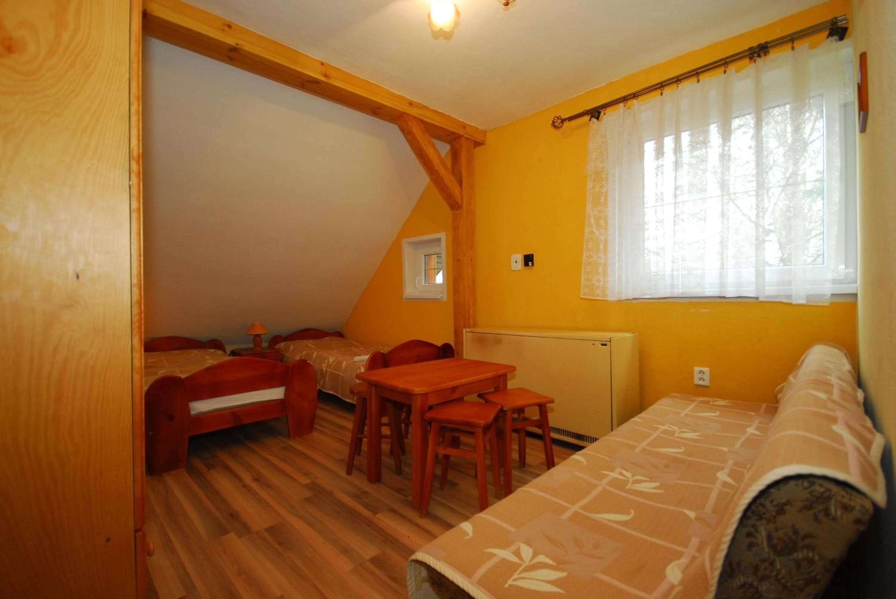 Habitació acollidora amb teulada inclinada, bigues de fusta, un llit, una taula i una cadira.