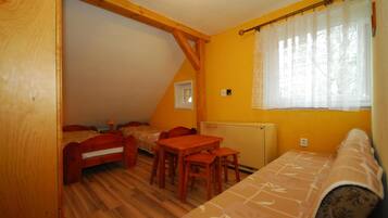 Habitació acollidora amb teulada inclinada, bigues de fusta, un llit, una taula i una cadira.