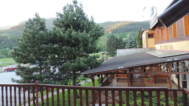 A wooden balcony with a view of a mountain and a river. - Penzión Western (Ruzomberok)