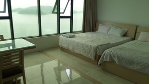 A hotel room with a bed, a desk, and a view of the sea.