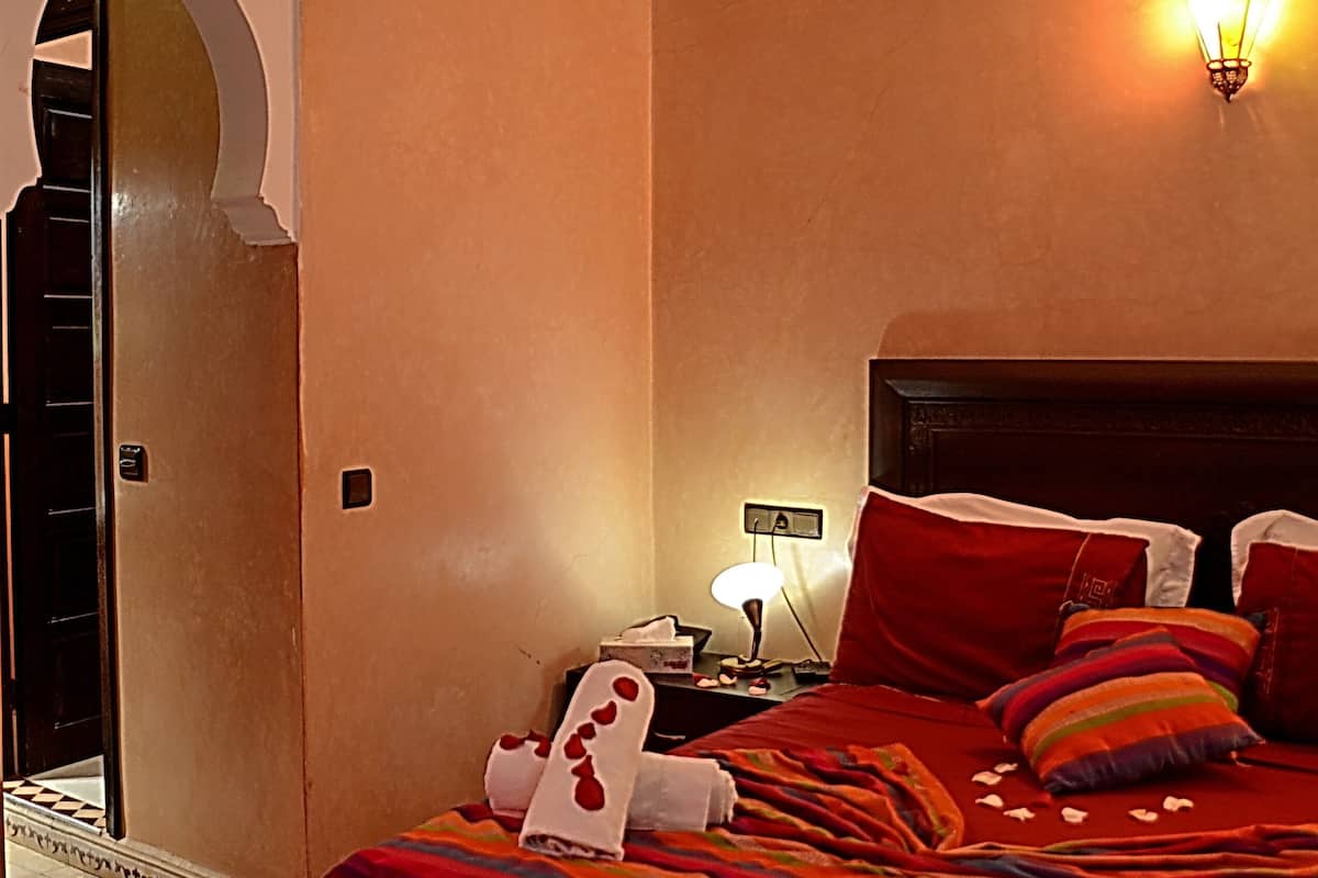 Une chambre d’hôtel avec un grand lit, une table de chevet, une lampe fixée au mur et un luminaire décoratif au plafond.