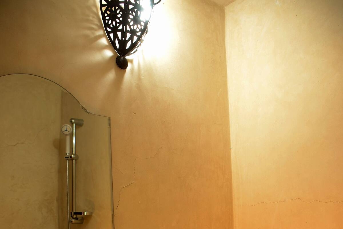 Une salle de bain avec un lavabo, des toilettes et une douche. Un miroir est placé au-dessus du lavabo et un luminaire décoratif est fixé au mur.