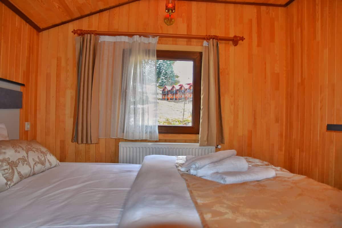 A wooden-paneled room with a bed, a window with curtains, and a view of a building outside.