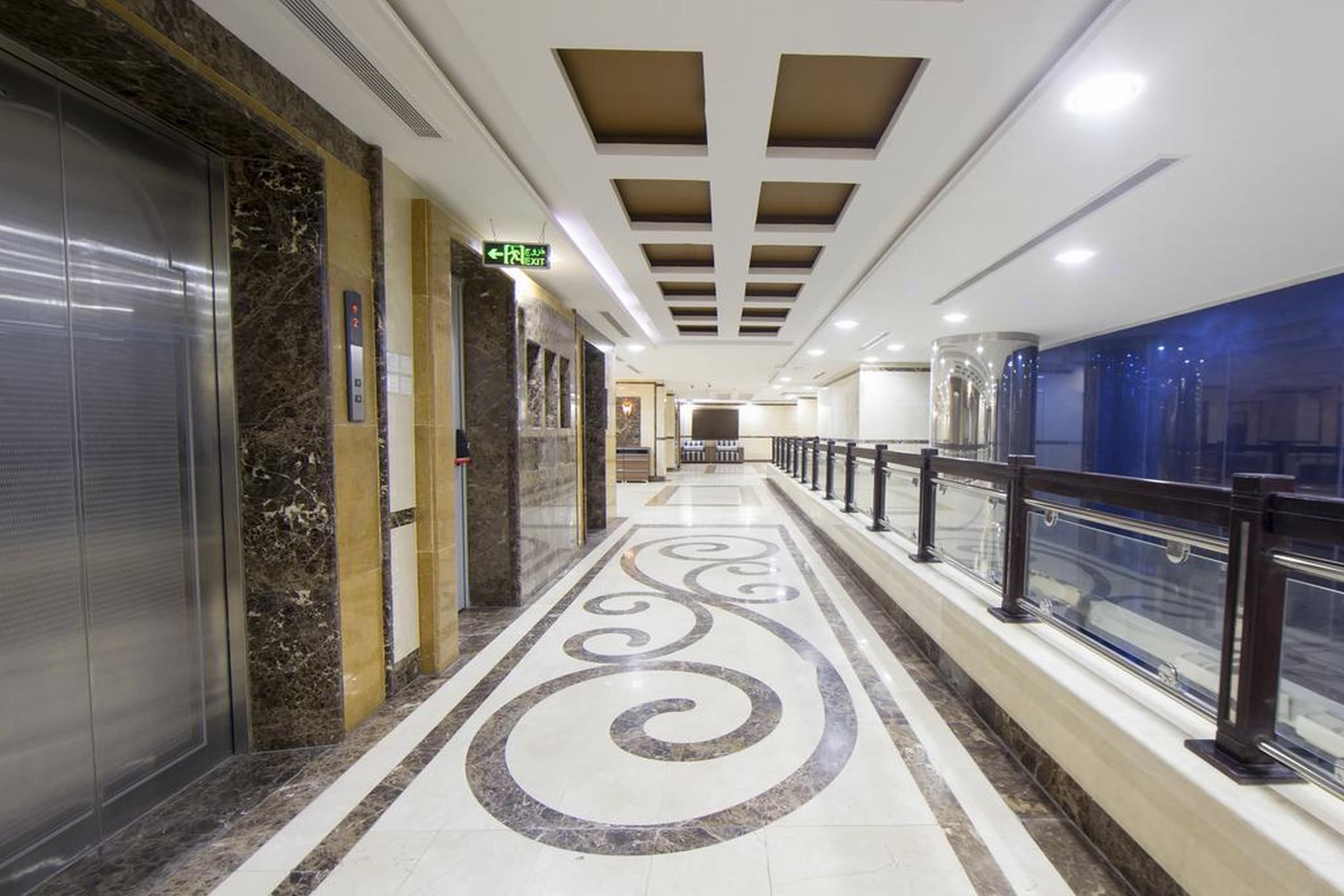 A corridor with marble flooring, a glass railing, and an elevator on the left.