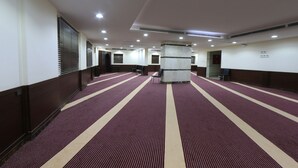 A hotel corridor with a patterned carpet, a central pillar, and multiple doors along the walls.
