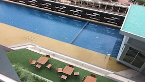 Ein Schwimmbecken mit gefliestem Sonnendeck, umgeben von einer Rasenfläche mit Holztischen und -stühlen.