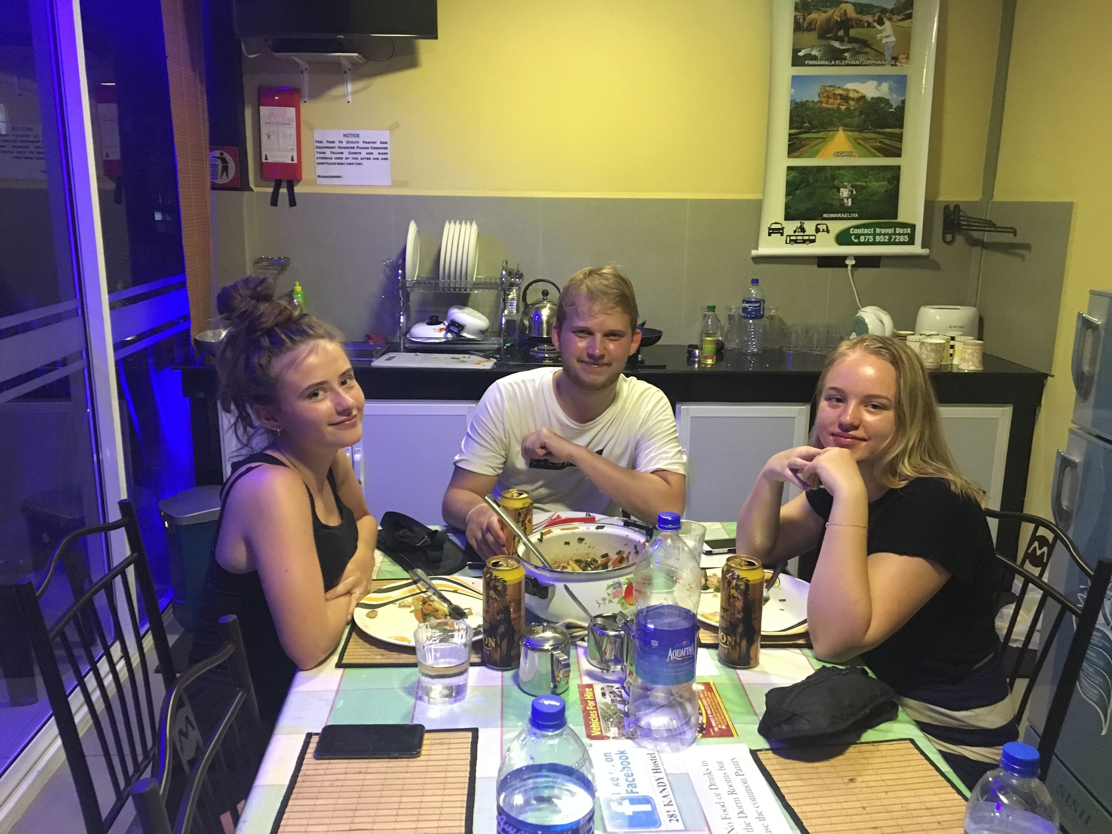 Un comedor con una mesa preparada para tres personas, un refrigerador, un lavabo y un panel de menú en la pared.
