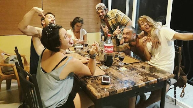 A group of people sitting around a wooden table with drinks, including a bottle of Coca-Cola, in a room with wooden paneling and a large window. - Kandy City Rooms & Hostel (Kandy)