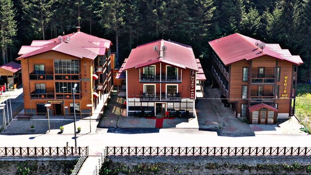 Un hotel con techo rojo y fachada de piedra, rodeado de un bosque.