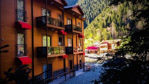Un edificio de madera de varios pisos con balcones, un patio de grava y montañas al fondo.