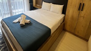 Habitación de hotel con una cama grande, un armario de madera, una mesita de noche con espejo y vistas a la vegetación desde la ventana.