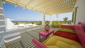A covered outdoor seating area with a view of the ocean, white furniture, and a table with a lantern. - Villa Agrikoia (Santorini)