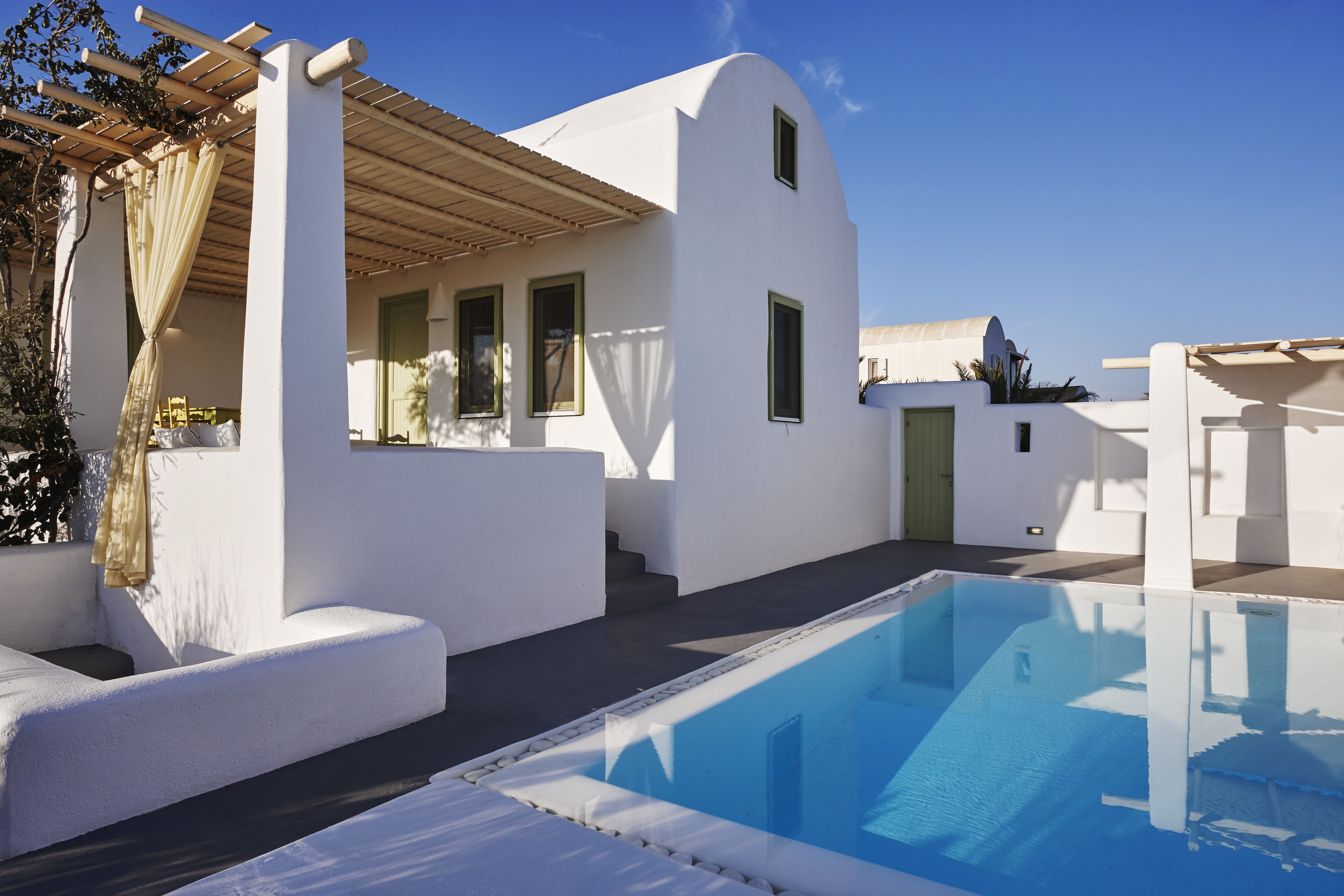 Une villa moderne aux murs blancs, dotée d’une piscine, d’une pergola et surplombant un ciel d’un bleu limpide.