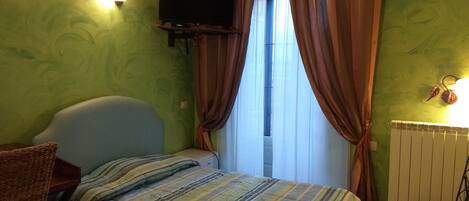 Un dormitorio con una cama, un televisor montado en la pared y una ventana con cortinas.