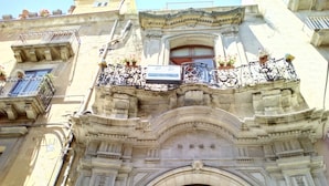 Un edificio histórico con balcones ornamentados, una gran entrada en arco y una puerta de hierro forjado decorativa.