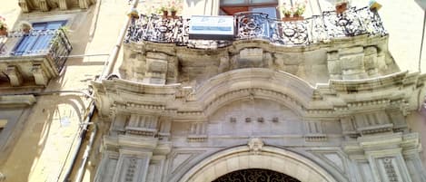 A historic building with ornate balconies, a large arched entrance, and a decorative wrought iron gate.