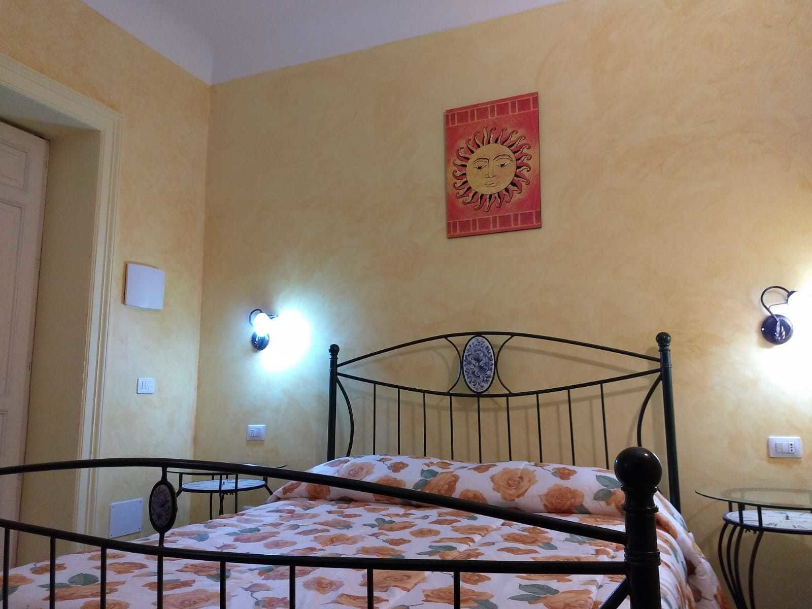 Quarto com cama, luminária na parede, mesinha e um adorno de parede.