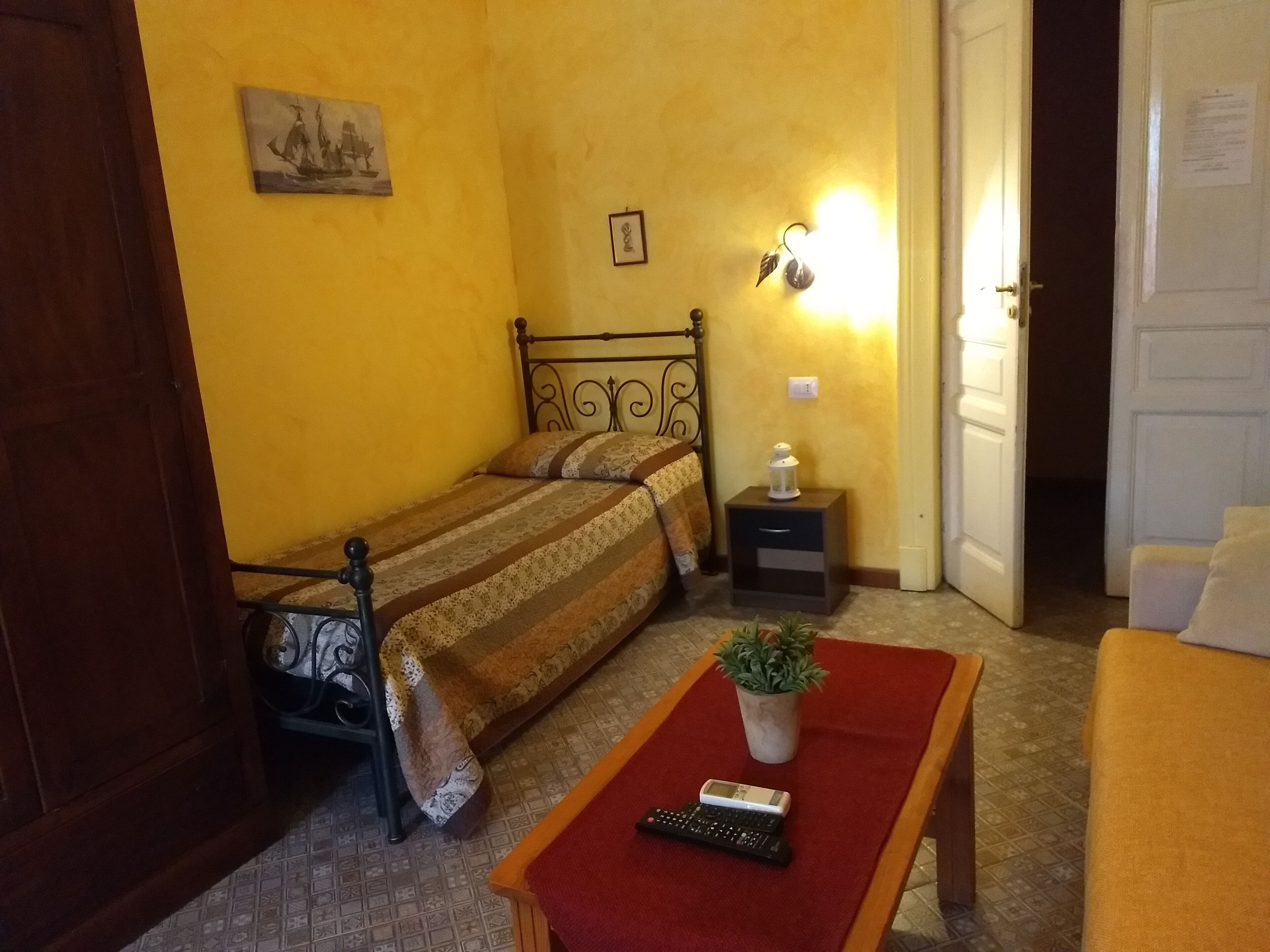 A bedroom with a bed, bedside table, lamp, and a small potted plant.