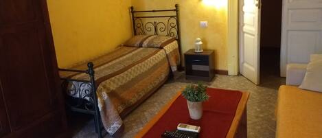 Un dormitorio con cama, mesita de noche, lámpara y una pequeña planta en maceta.