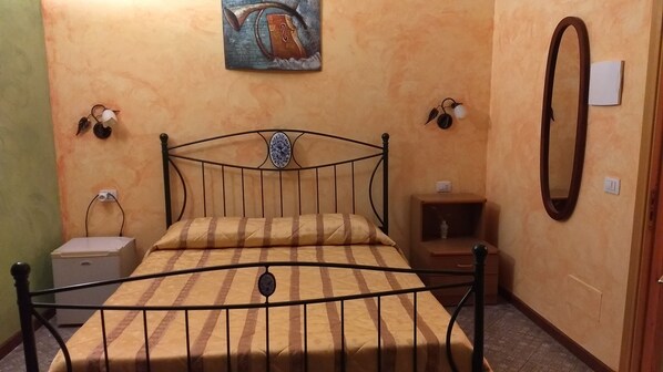A bedroom with a metal bed frame, a bedside table, a nightstand, a wall-mounted mirror, and a painting on the wall.